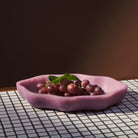 Pink serving dish filled with red grapes on checkered placemat showing functional use