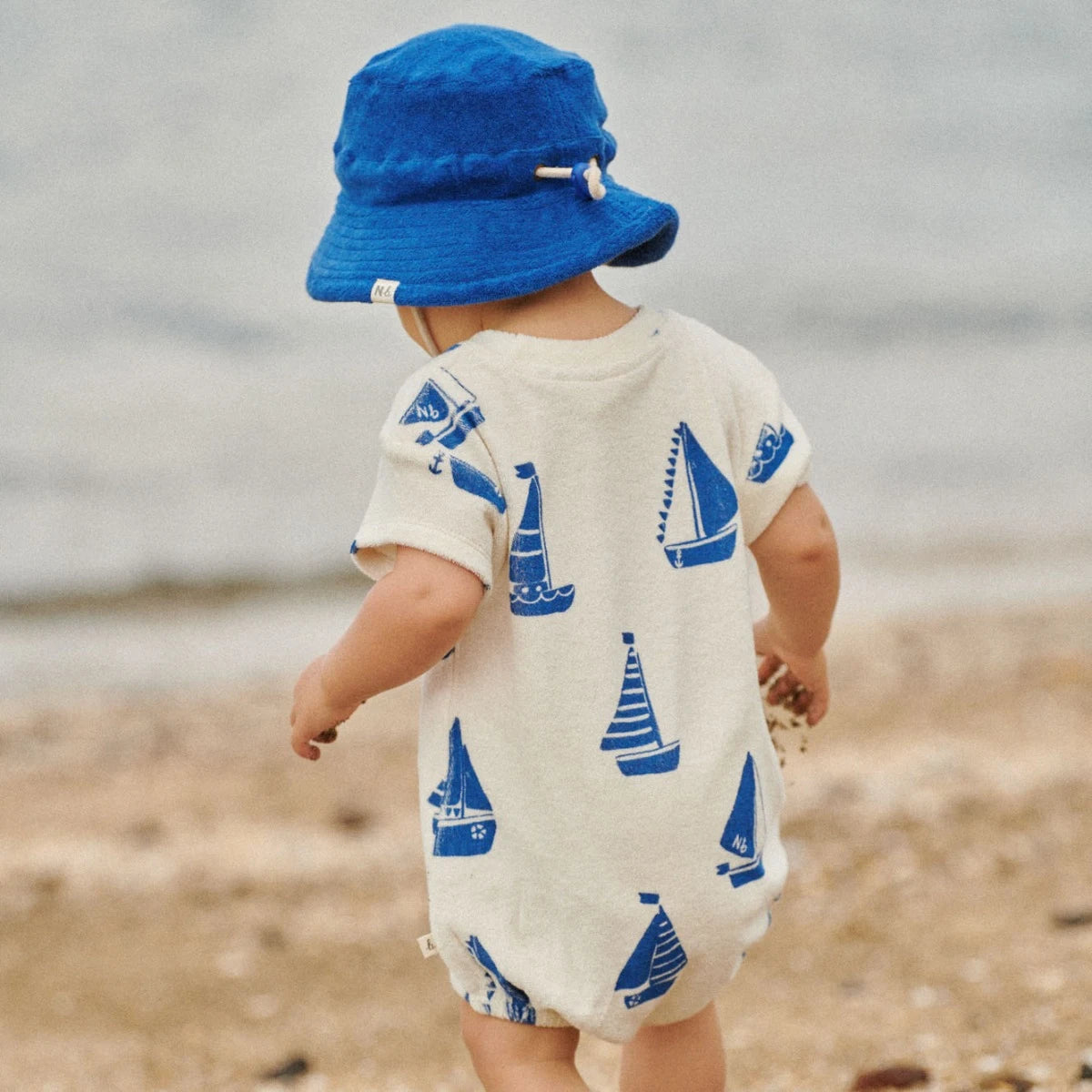 boy wearing Juno Romper Terry Regatta Print by Nature Baby - cream organic terry romper with blue sailing boats