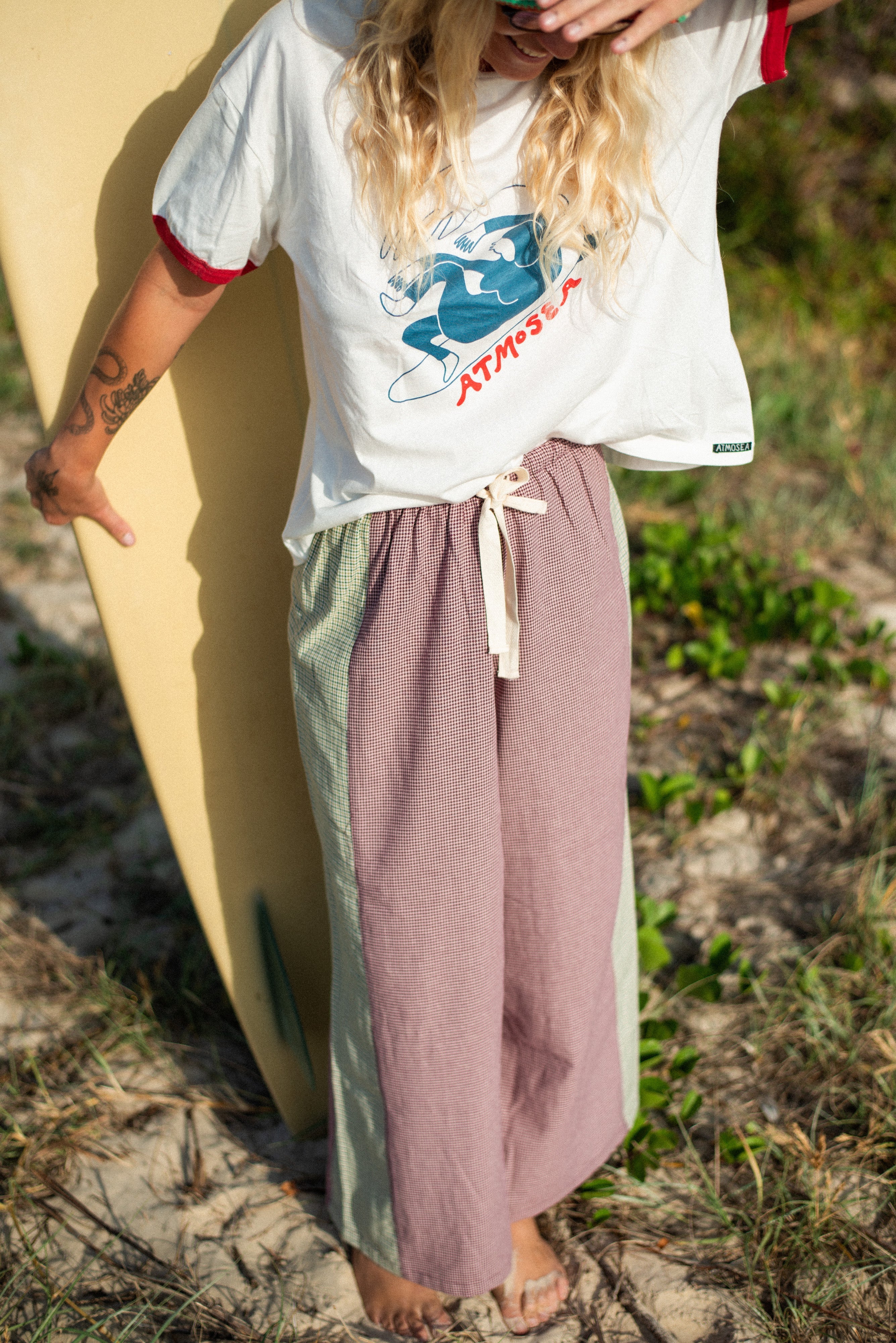 Beach lifestyle shot of woman in Atmosea Patchwork Pant Houndstooth Combo with surfboard
