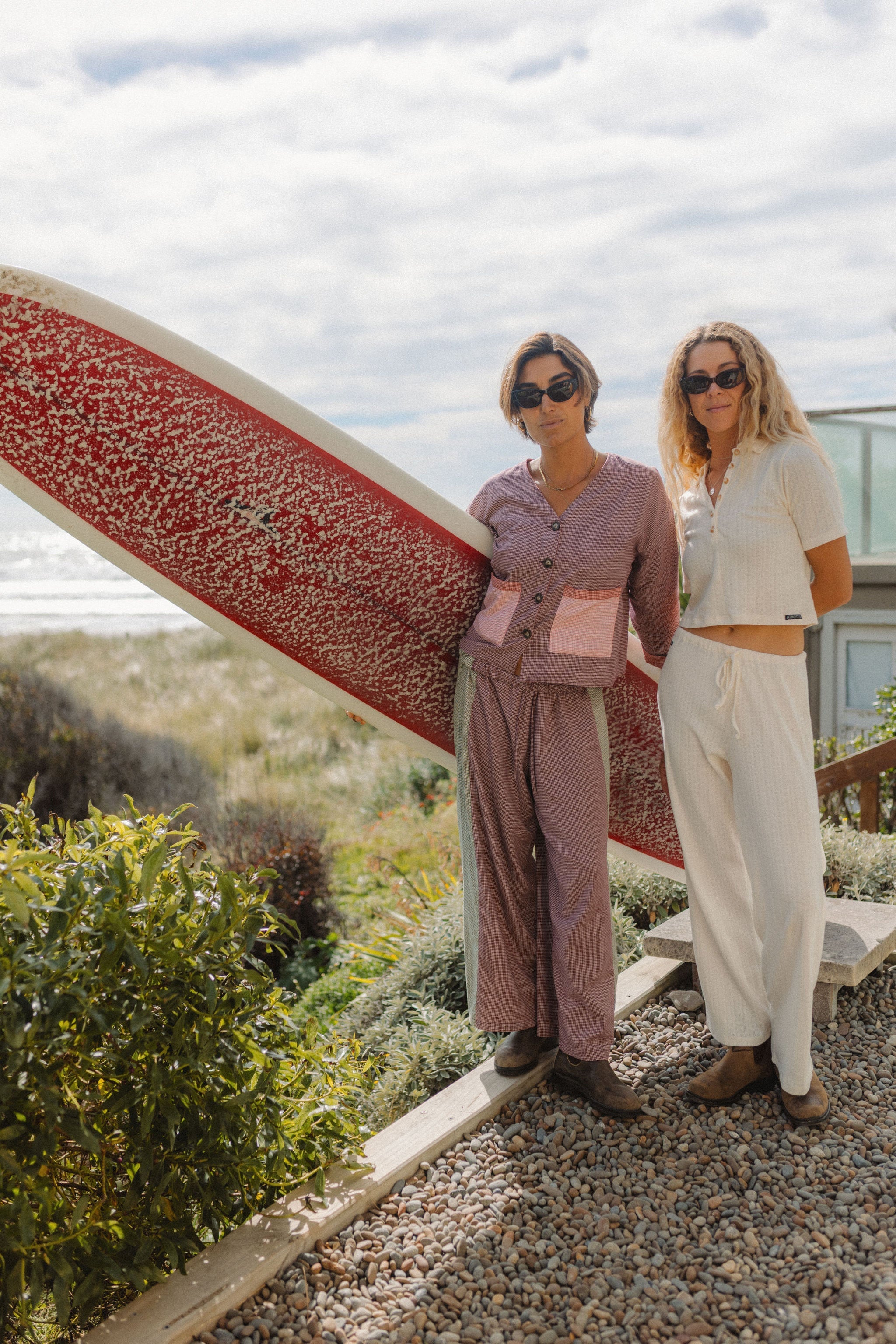 Two women modeling Atmosea Patchwork Pant Houndstooth Combo in coastal setting with surfboard