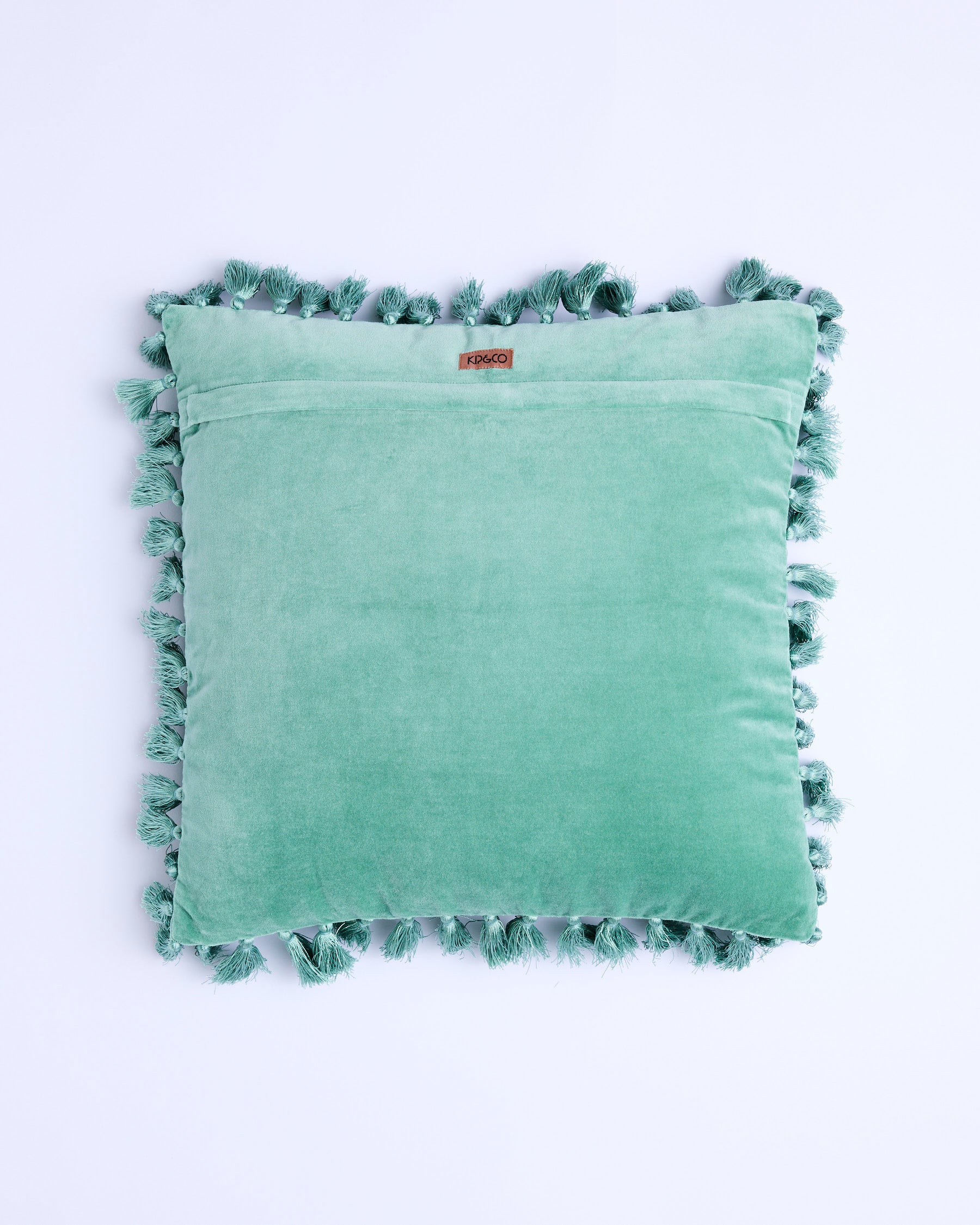 Back view of pistachio velvet tassel cushion showing brand label and tassel trim detail