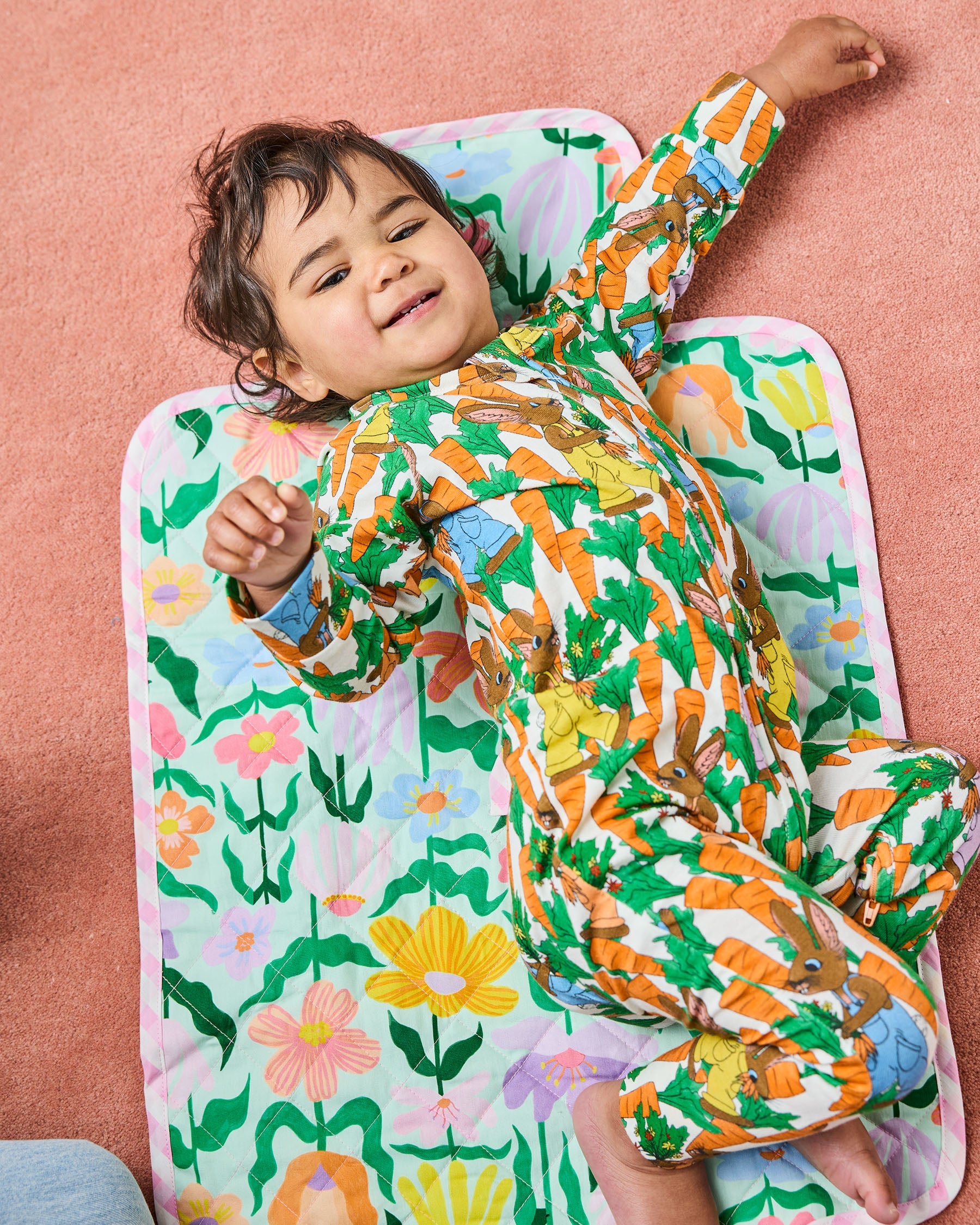 Child lying on Kip Co Popping Flowers Green Baby Change Mat showing colorful floral pattern and full mat size