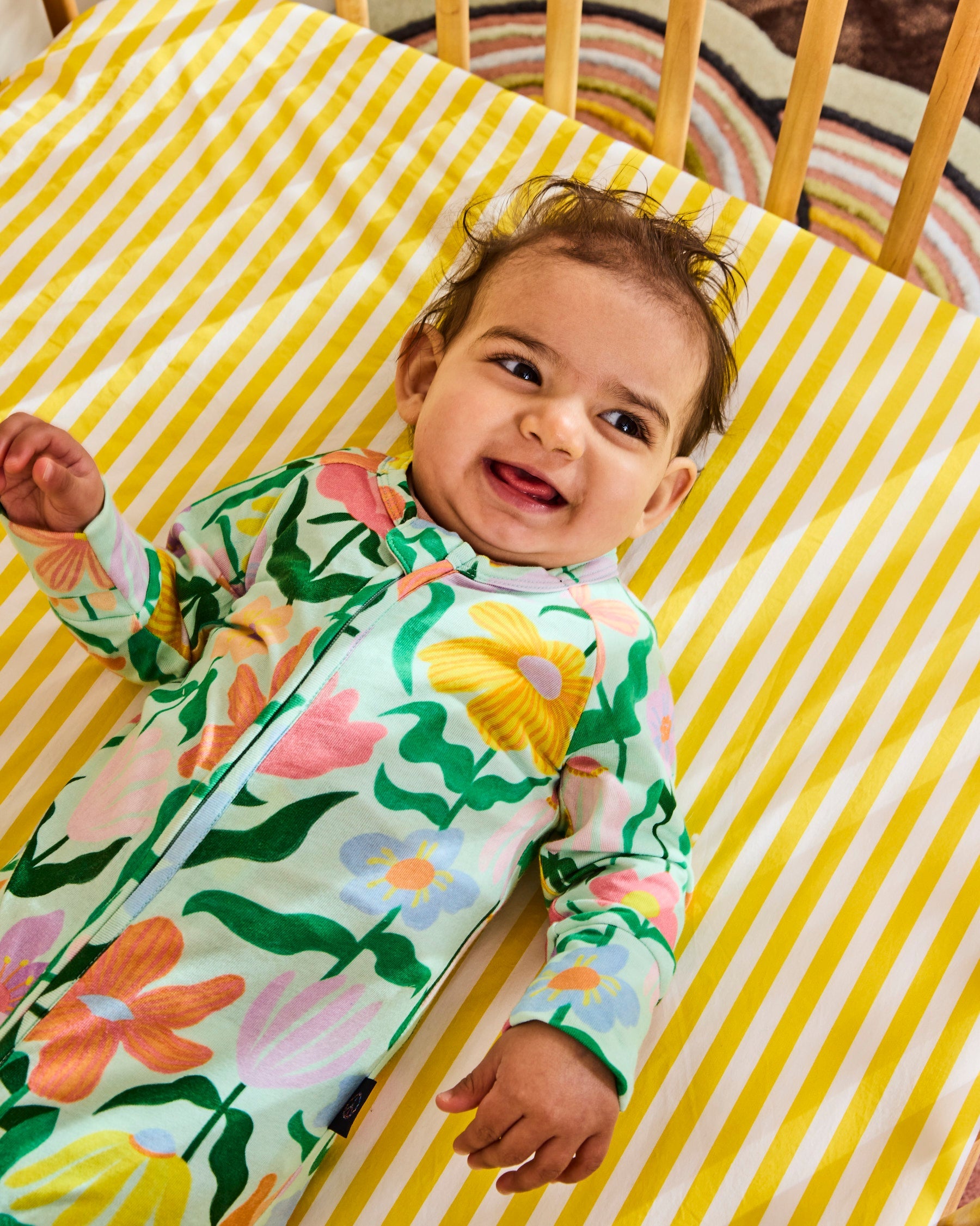 Baby lying in crib wearing Kip & Co Popping Flowers Green Organic Zip Romper on yellow striped sheet