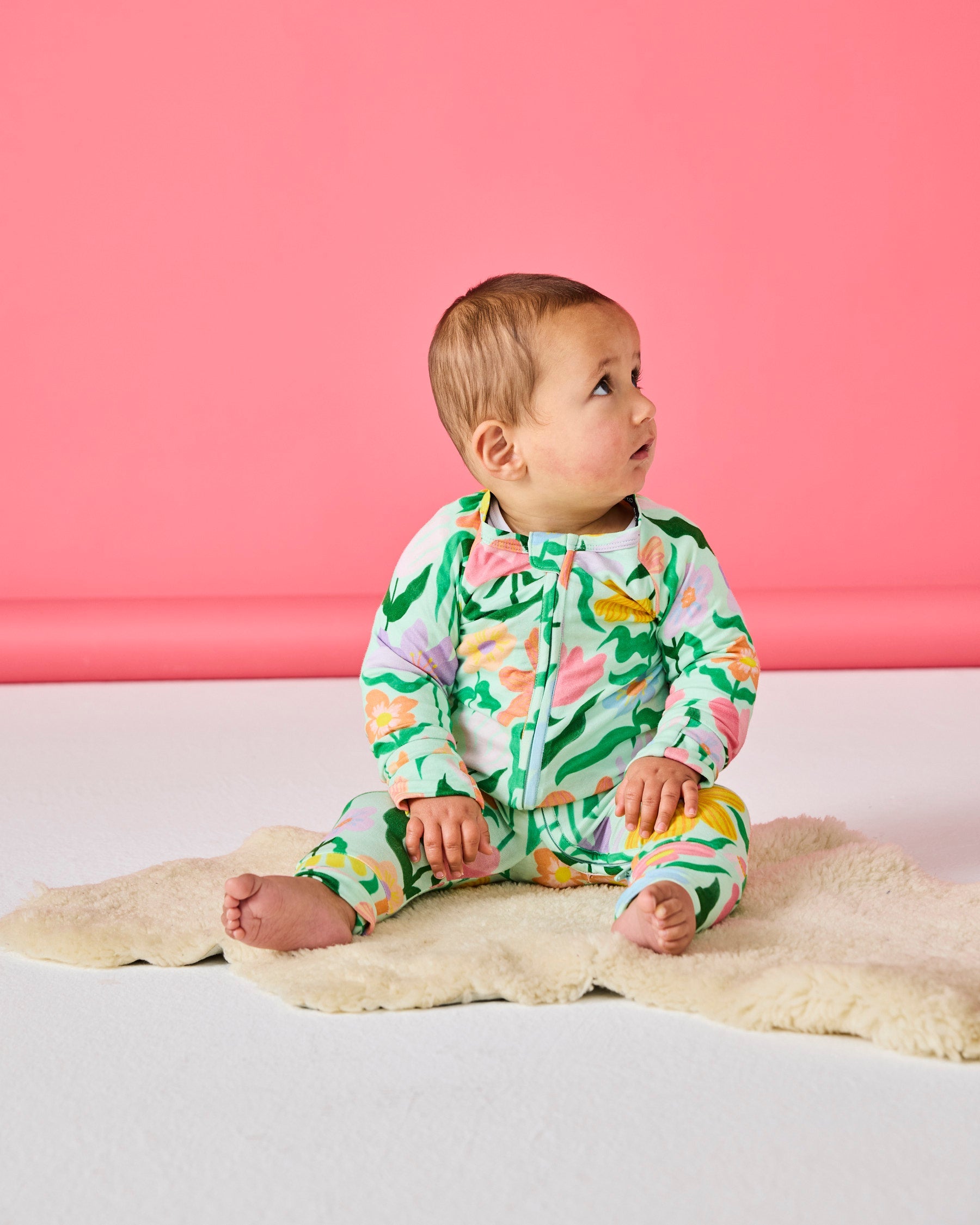 Side profile of baby sitting on sheepskin rug wearing Popping Flowers Green Long Sleeve Zip Romper