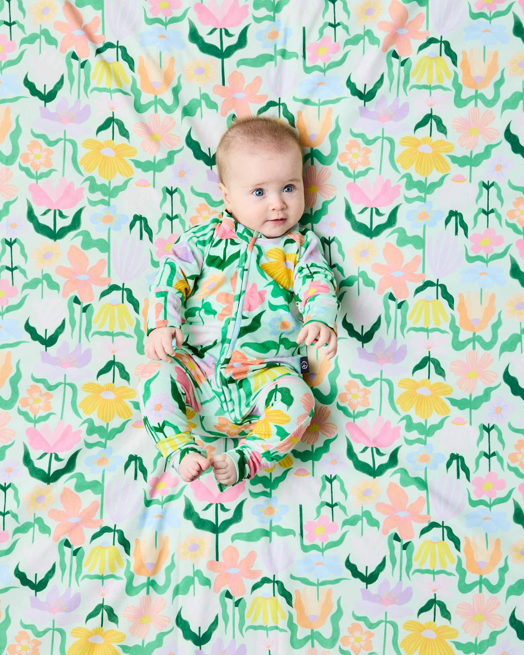Baby positioned on matching Popping Flowers Green fabric background wearing Kip & Co Organic Zip Romper