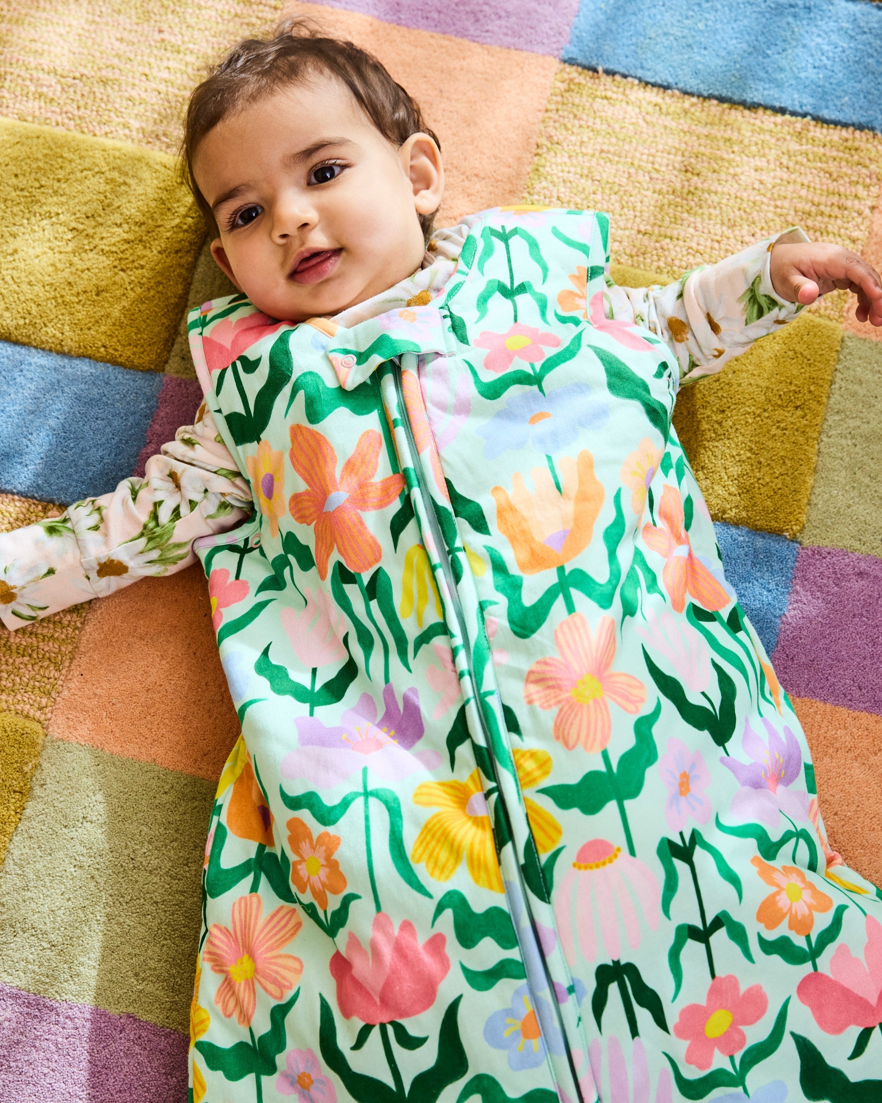 Baby wearing Kip & Co Popping Flowers Green Sleep Bag 2.5 Tog on colorful geometric rug