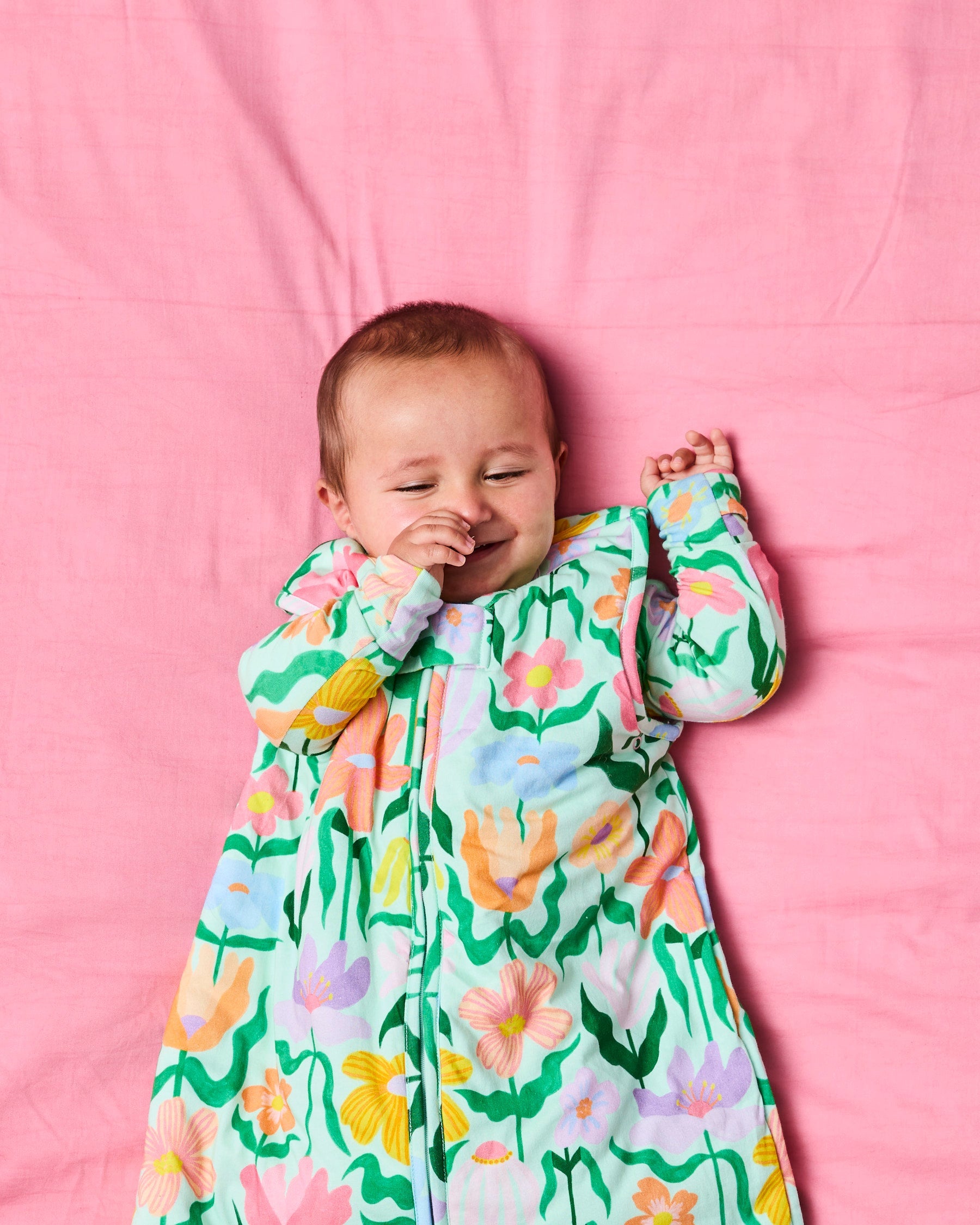 Baby in Kip & Co sleep bag with colorful floral print on pink bedding background