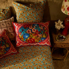 Red floral silk pillowcase styled on a bed with mixed print bedding and a wicker nightstand