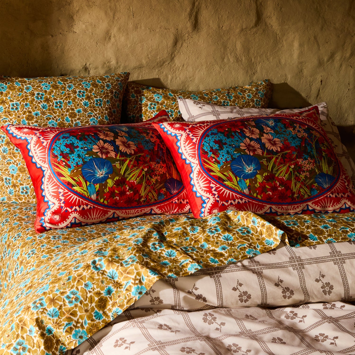 Pair of red floral silk pillowcases with oval medallion design styled on a boho-layered bed