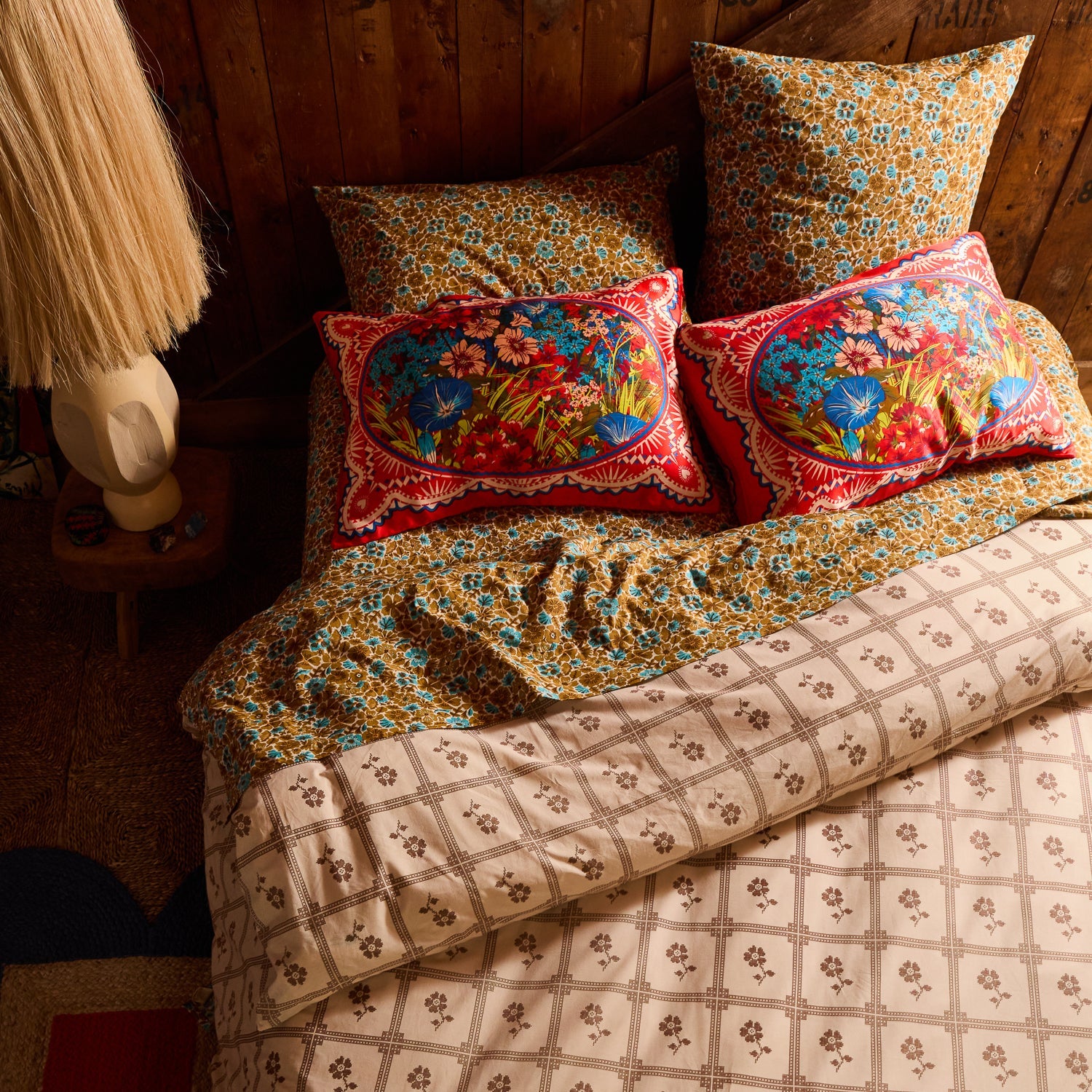 Two red floral silk pillowcases with oval bouquet print on a rustic wood-panelled bedroom bed