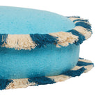 Side angle detail of a turquoise round cushion showing the alternating teal and cream fringe trim