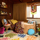 Turquoise round fringe cushion styled on the floor of a boho bedroom beside a patterned bed