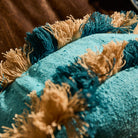 Close-up detail of the teal and natural cream alternating fringe trim on a turquoise round cushion