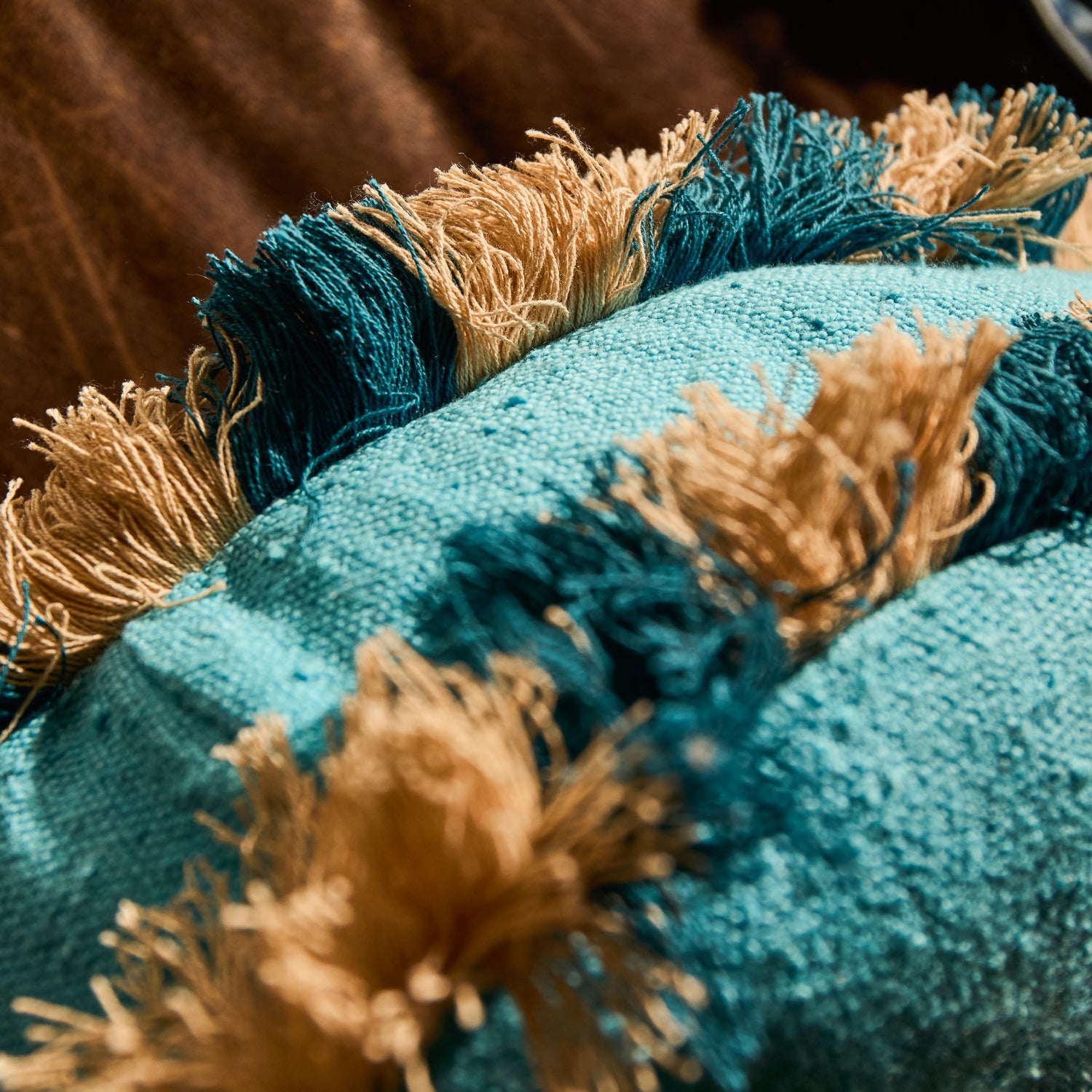 Close-up detail of the teal and natural cream alternating fringe trim on a turquoise round cushion