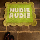 Cactus Green Nudie Rudie bath mat with scalloped border laid on stone tile floor, overhead angle