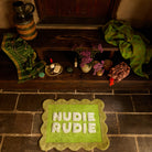 Cactus Green Nudie Rudie bath mat on stone floor styled with bathroom accessories on a wooden bench above
