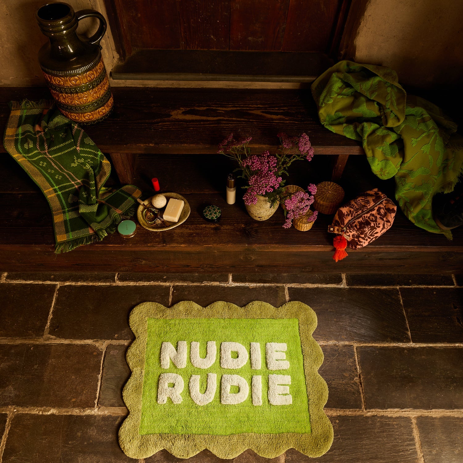 Cactus Green Nudie Rudie bath mat on stone floor styled with bathroom accessories on a wooden bench above