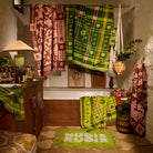 Cactus Green Nudie Rudie bath mat on a jute rug in a richly styled bathroom with hanging towels