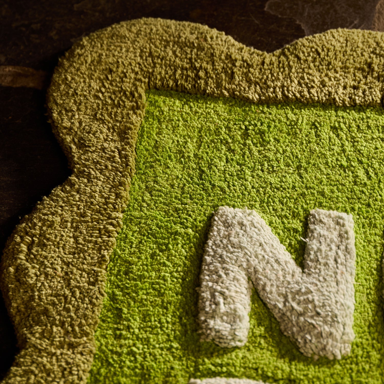 Close-up detail of the Cactus Green Nudie Rudie bath mat showing tufted texture, scalloped edge and white letter N