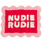Poppy Nudie Rudie bath mat with scalloped pink border and bold red centre, white tufted lettering, flat-lay view