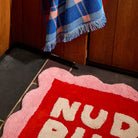Close-up corner detail of the Poppy Nudie Rudie bath mat showing red and pink scalloped tufted texture on tile floor