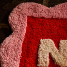 Close-up detail of the Poppy Nudie Rudie bath mat showing plush red and pink scalloped tufted construction