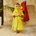Child wearing Rosalia Kids Poncho in Dune by Sage & Clare with tropical floral print and fringed edges