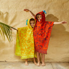 Two children wearing Rosalia Kids Ponchos showing vibrant yellow and red colorways with fringed edges