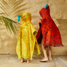 Back view of two children in terry towelling hooded ponchos with tropical print designs