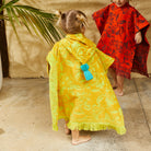 Back view of children wearing Rosalia Kids Ponchos showing hood details and colorful tassel accents