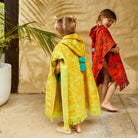 Rear angle of kids in terry cotton hooded ponchos displaying fringed hem and tropical leaf patterns