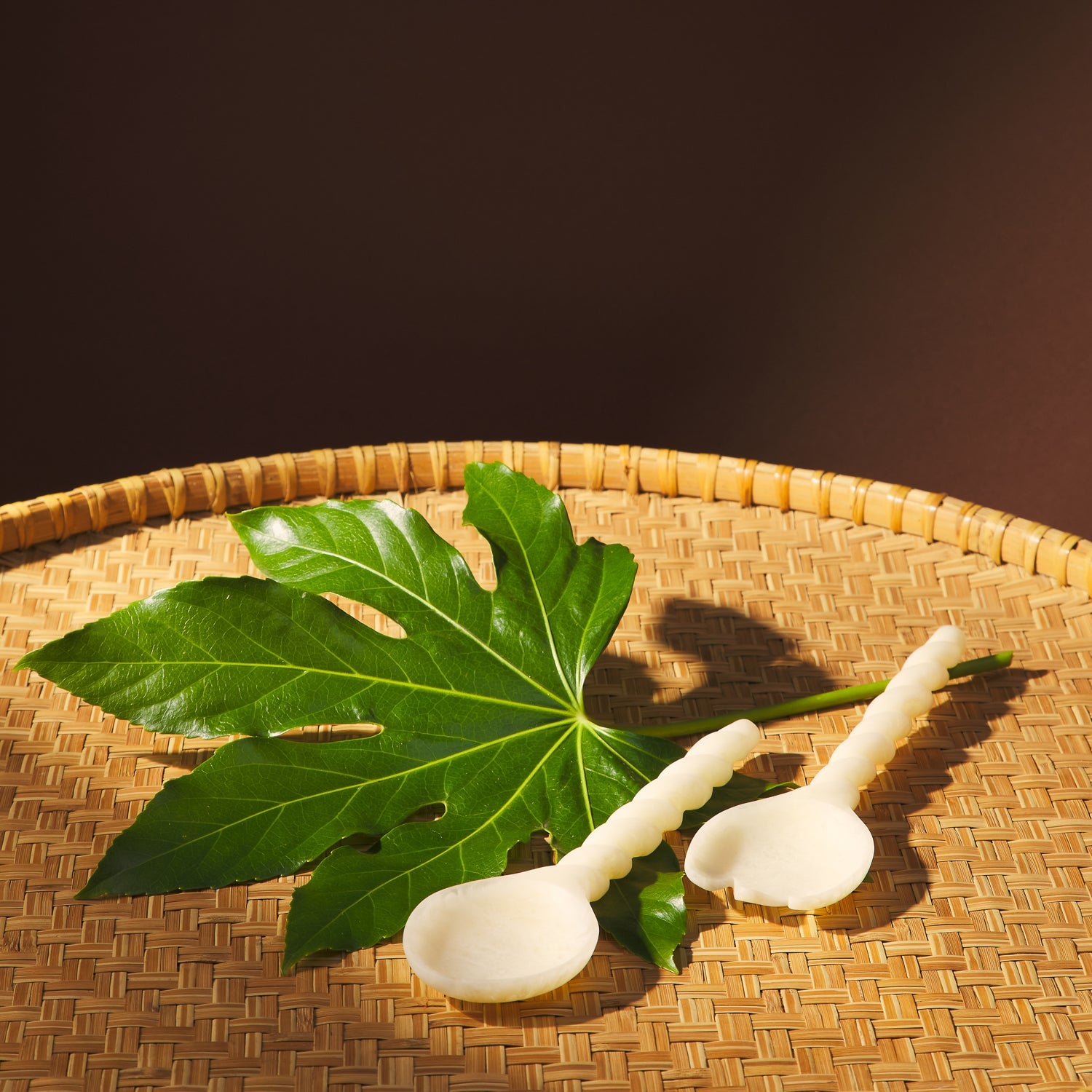 Pearl rose salad servers resting on a woven rattan tray alongside a tropical leaf