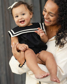 Front view of a baby girl in the Sailor Romper Black | Rylee + Cru