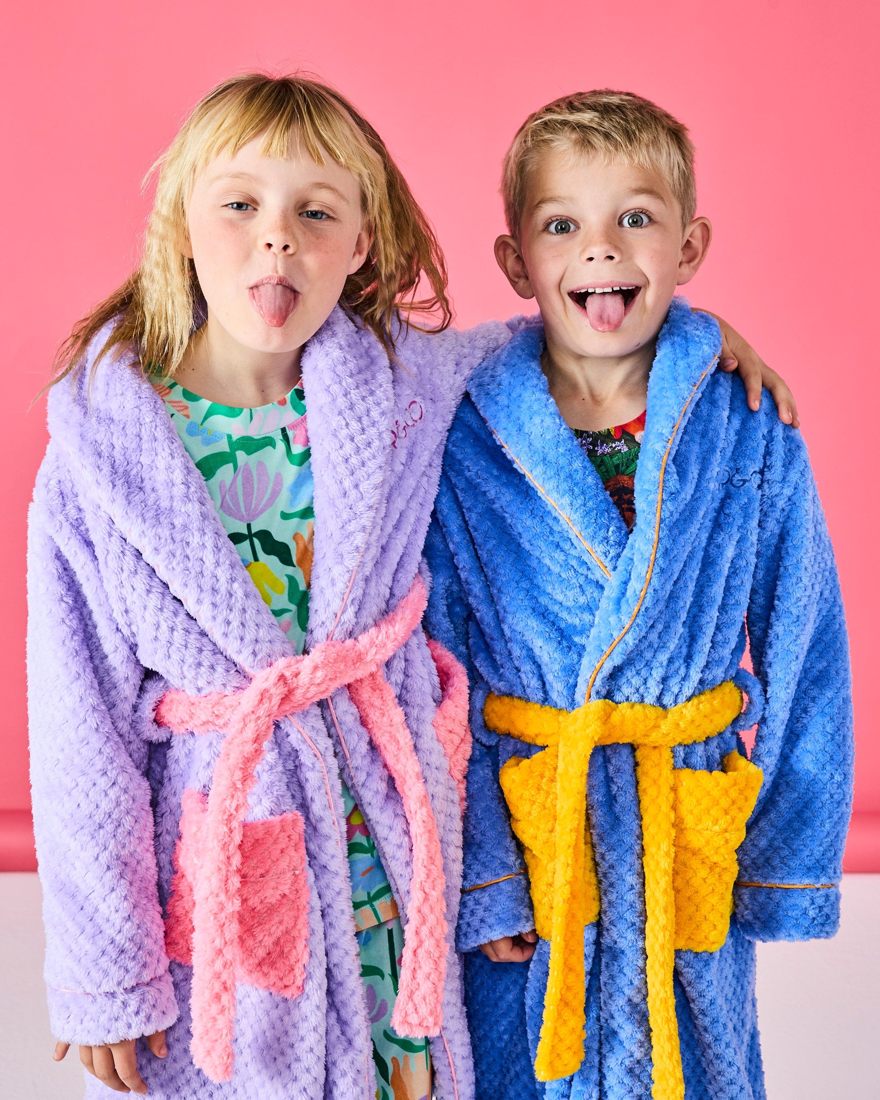 Two children wearing Kip & Co Seaside Kids Cosy Robes in blue and purple with yellow and pink belt ties