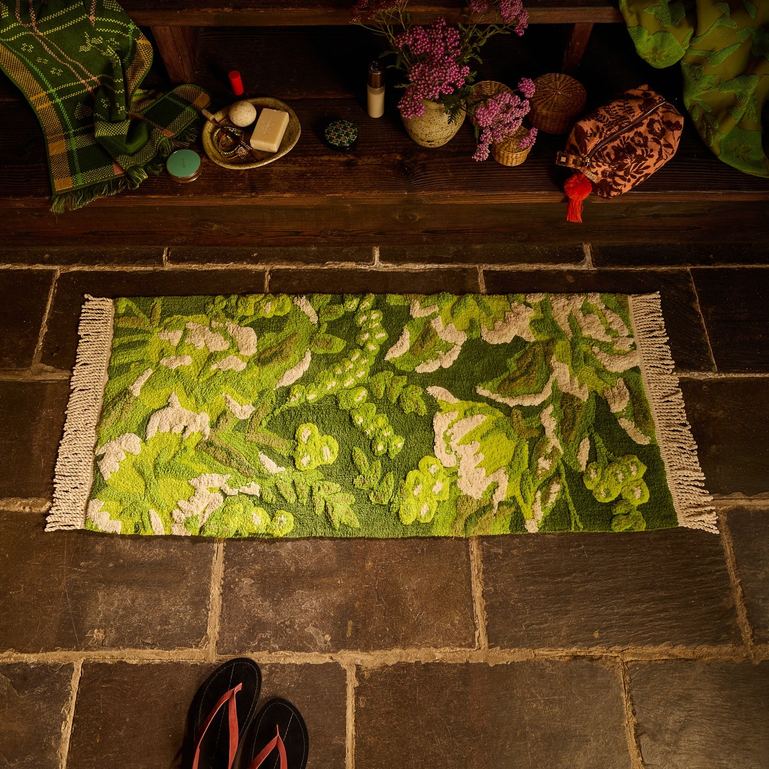 Green floral tufted bath runner with cream fringe on stone floor, styled with bathroom accessories and bench