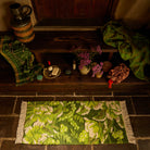 Overhead view of green floral tufted bath runner with cream fringe on stone floor beside a wooden bench