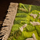 Close-up of bath runner corner showing twisted cream fringe and textured green floral tufted pile detail