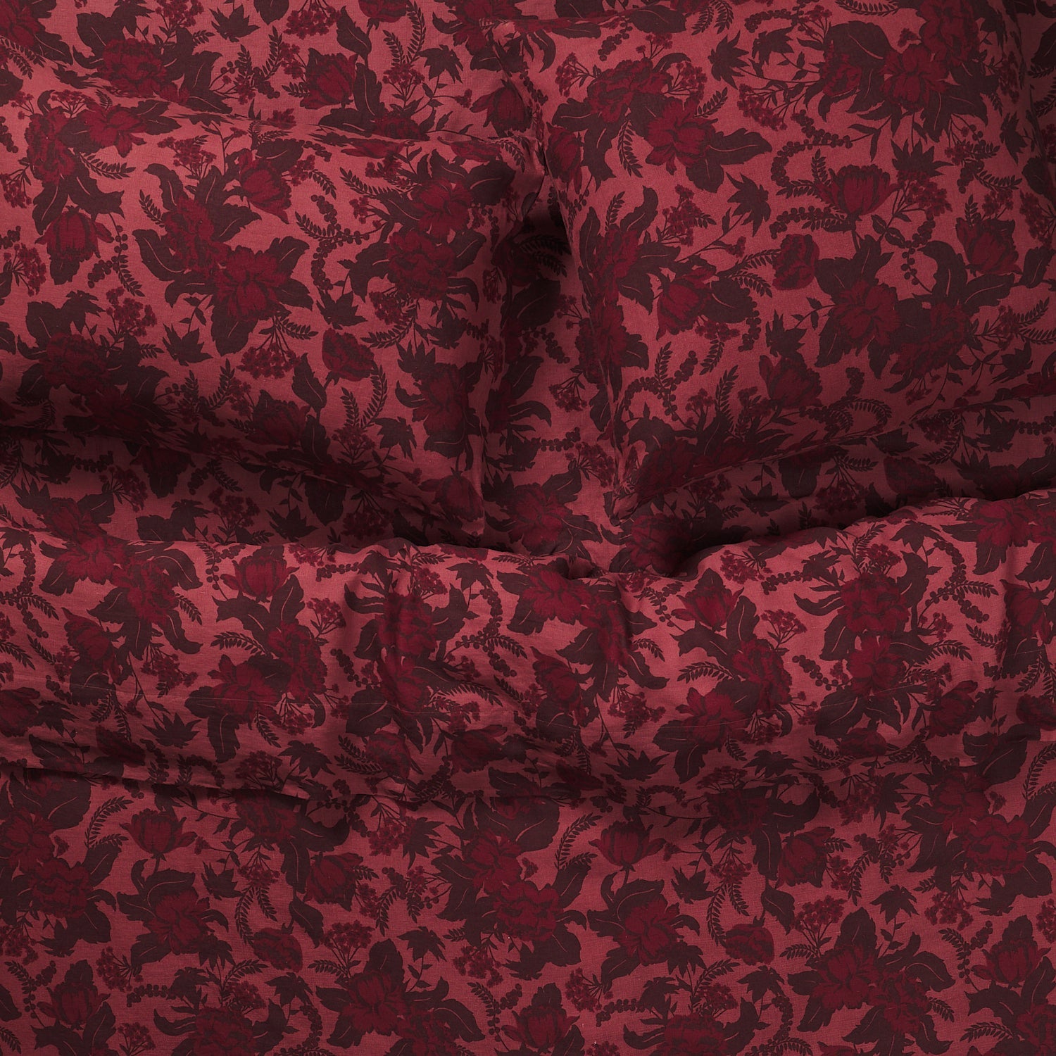 Close-up of deep red botanical floral linen pillowcases on a bed, showing texture and print detail