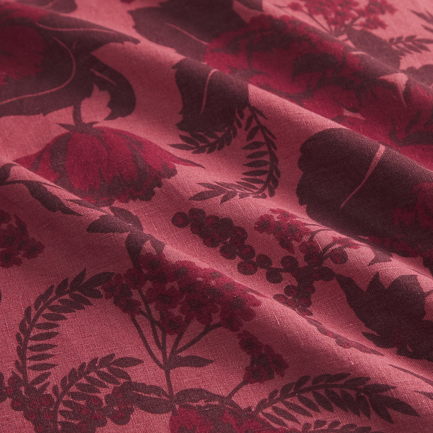 Macro detail of dark burgundy floral print on crimson linen fabric, showing weave and pattern