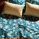 Overhead view of teal floral linen flat sheet draped across a styled bed with mixed-print pillows