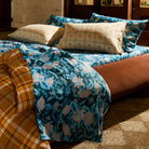 Teal blue floral linen flat sheet casually draped over a styled bed in a warm-lit bohemian bedroom