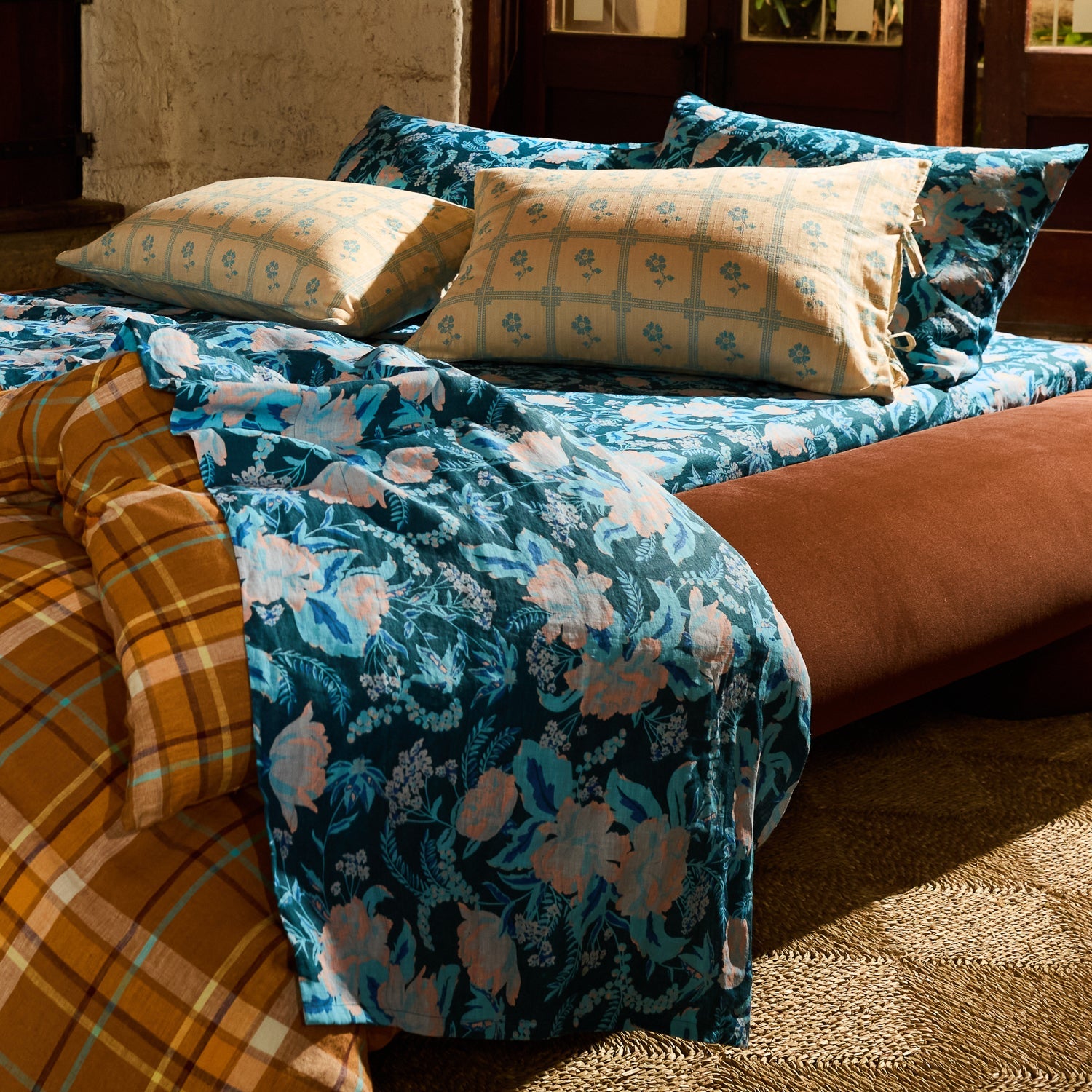 Teal blue floral linen flat sheet casually draped over a styled bed in a warm-lit bohemian bedroom