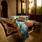 Teal floral linen sheet set styled on a bed in a rustic room with open doors to a tropical garden