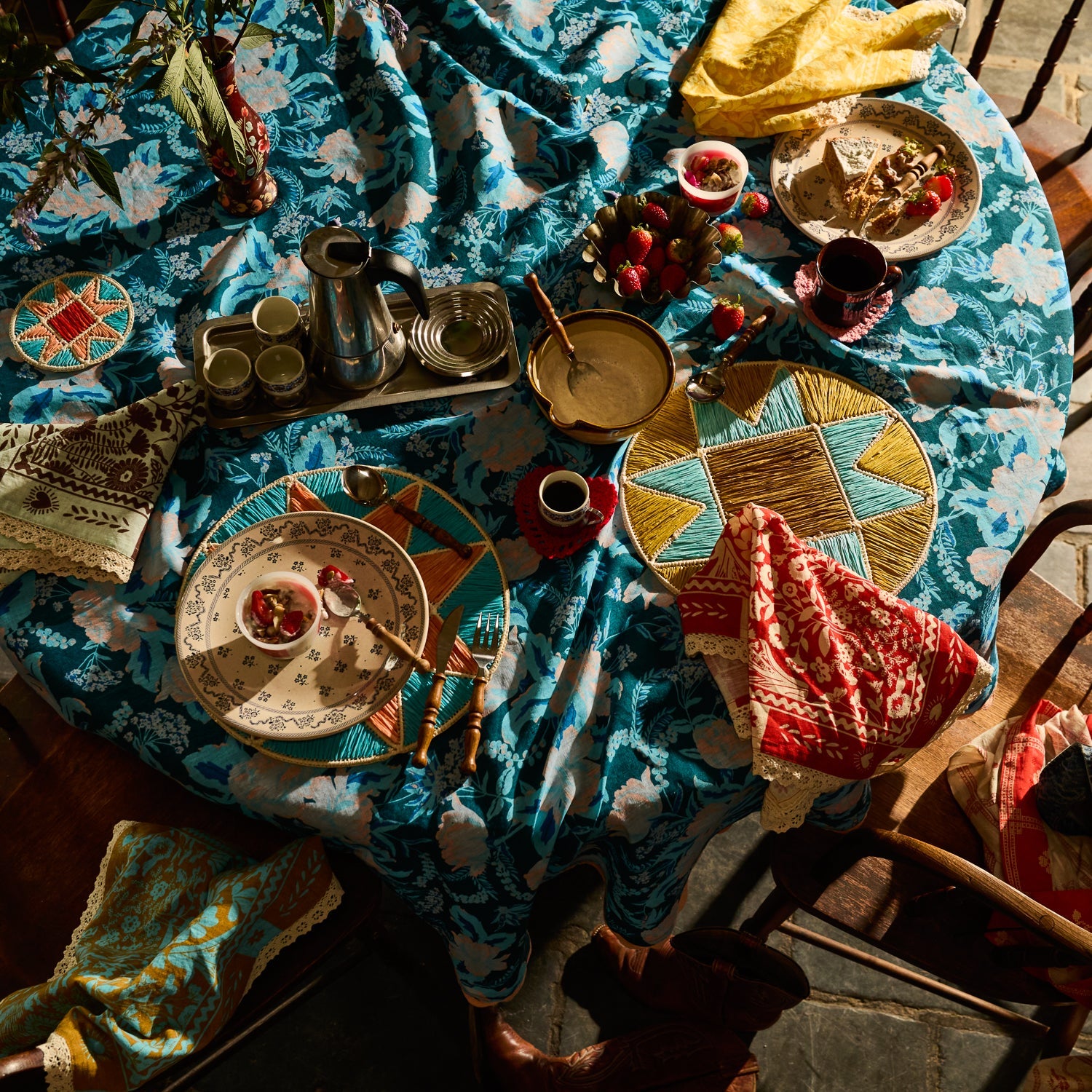 Overhead view of teal floral tablecloth on a set dining table with plates and food