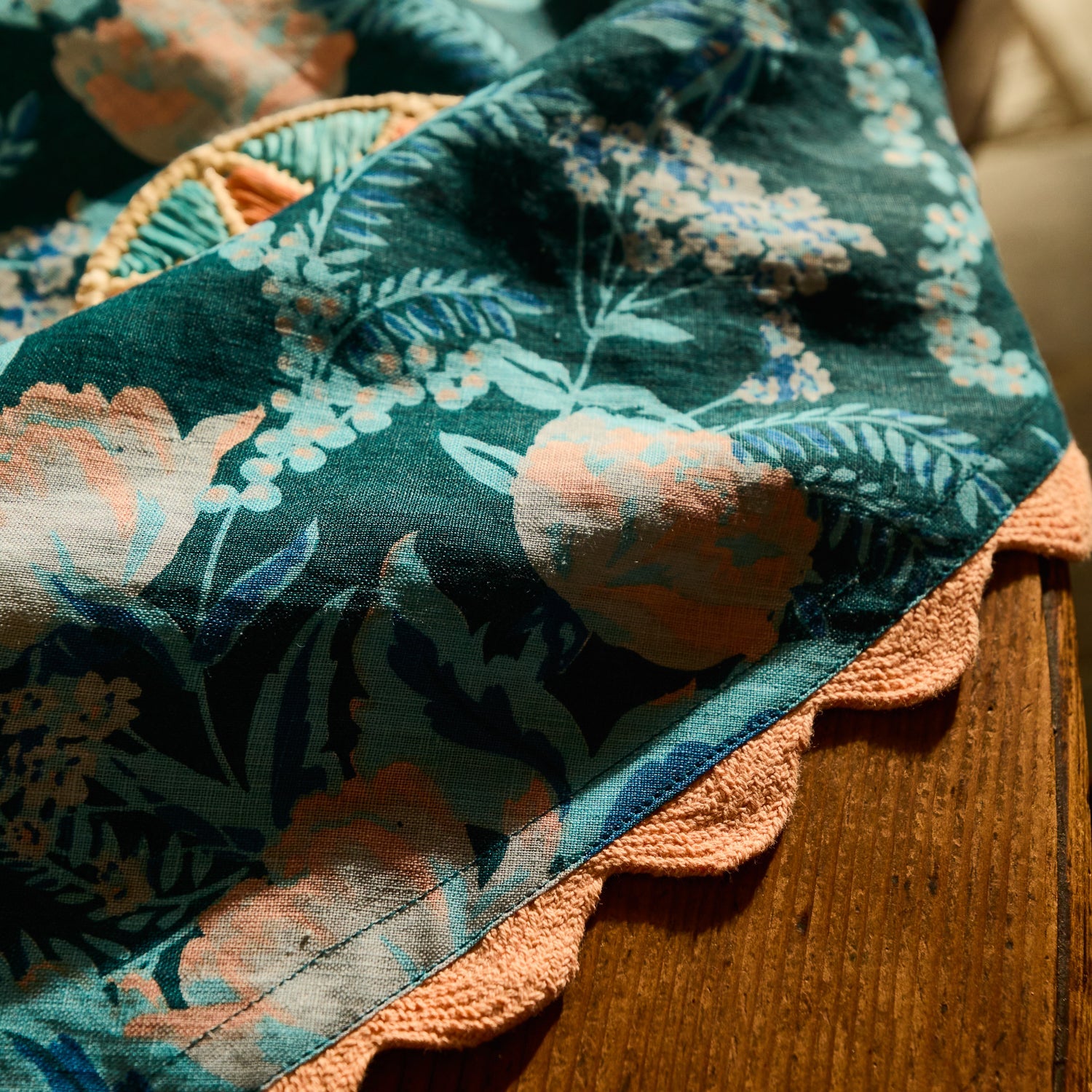 Close-up of teal and blush floral tablecloth fabric with peach scalloped border detail