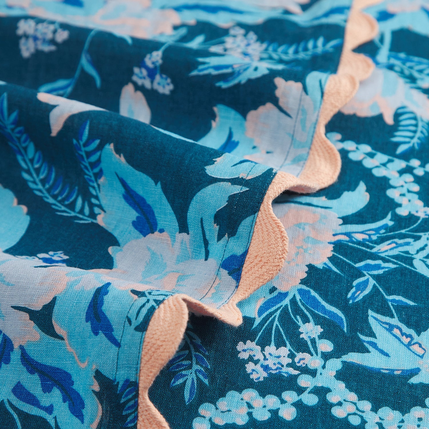 Macro detail of teal blue floral print tablecloth fabric with peach scalloped trim edge