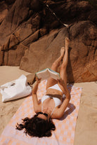 Woman reading a book on a towel by large rocks on a beach with Tyvek.beach bag