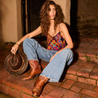 Vibrant multiprint satin cami top worn with wide-leg jeans and cowboy boots, seated pose