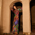 Full-length side view of a woman in a multicolour long-sleeve maxi dress standing in a stone archway
