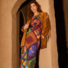 Woman wearing a multicolour patchwork-print maxi dress layered under a tan fringe suede jacket
